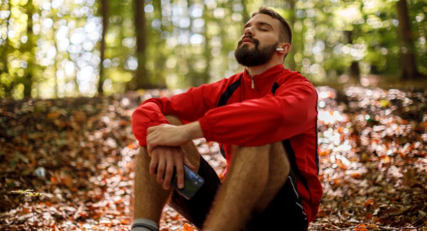 Portrait of relaxed young man with bluetooth headphones in forest 