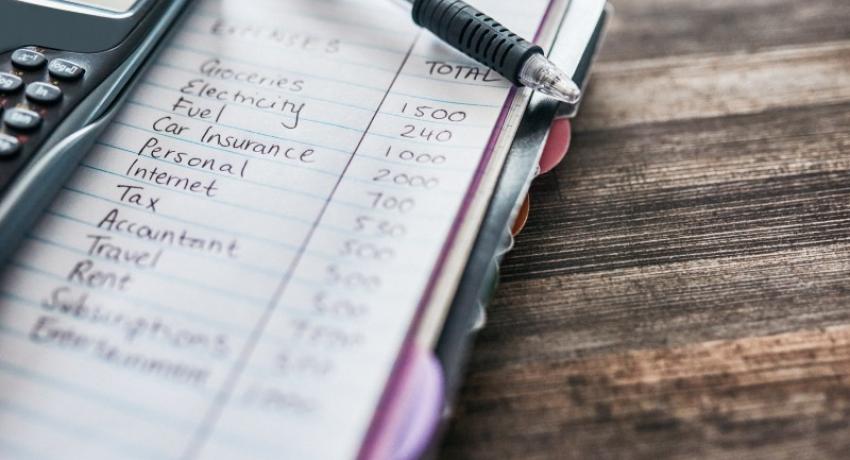 Shot of a notebook with a budget written on it and a calculator on a desk at home