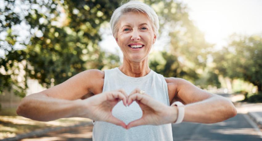 Fitness, happy and heart hands of old woman in nature after running for health, wellness and workout. Smile, motivation and peace with senior lady and sign for love, faith and training in nature